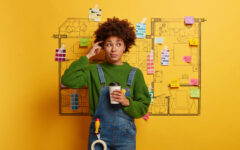 Professional hard working designer has thoughtful look, thinks about creative sketching project during coffee break, selects colors and furniture for new home interior of customers prepares house plan